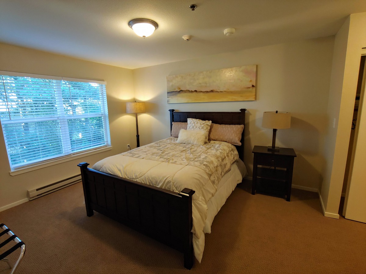 A cozy bedroom with a large bed, two nightstands with lamps, and a window letting in natural light.