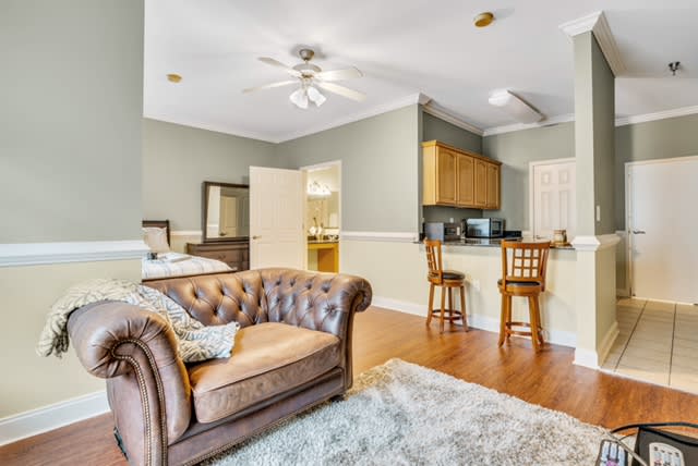A cozy living room with an open floor plan connecting to the kitchen, featuring a classic sofa, bar stools, and a ceiling fan.