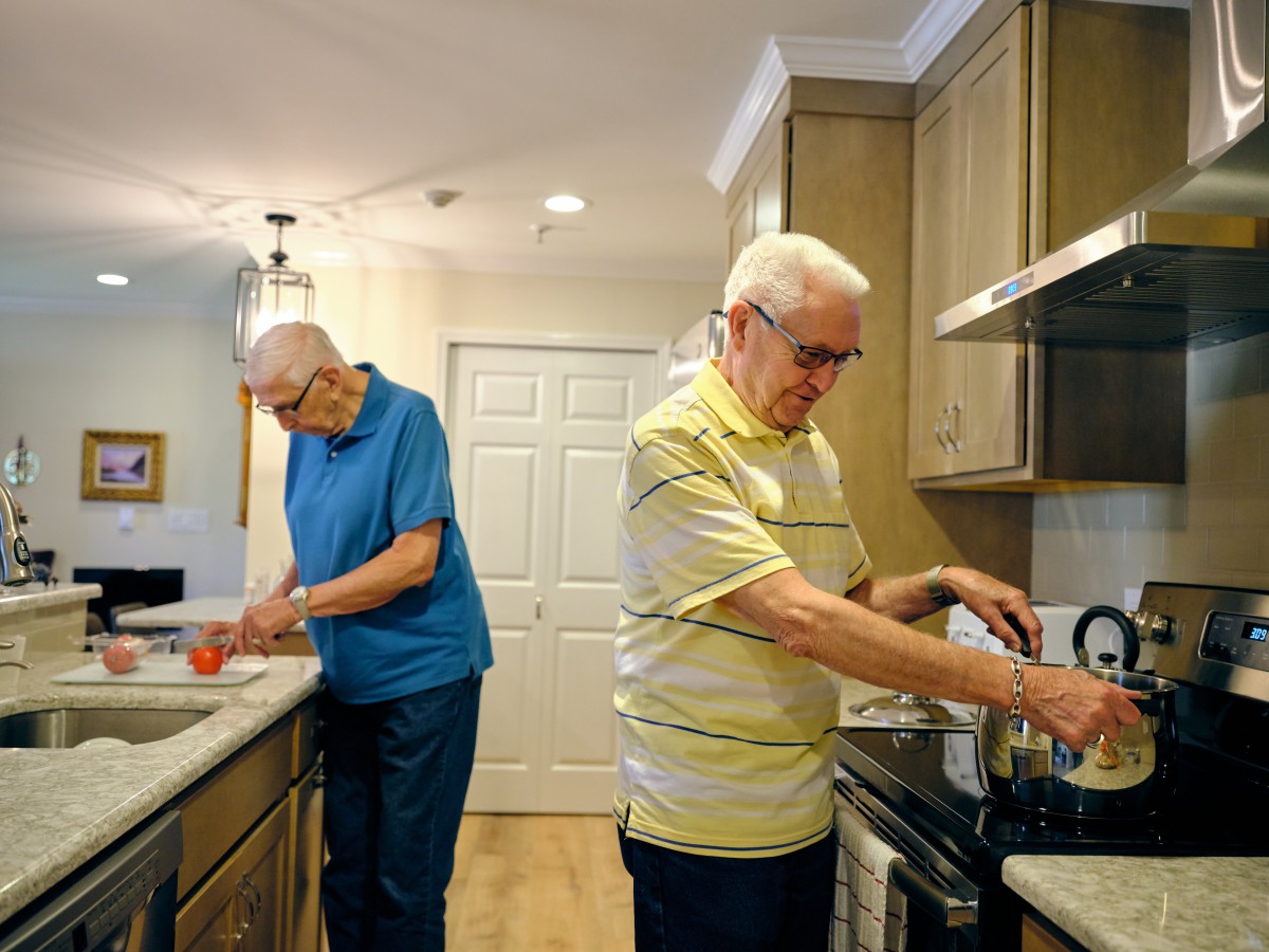 Two elderly men preparing food in a kitchen together.