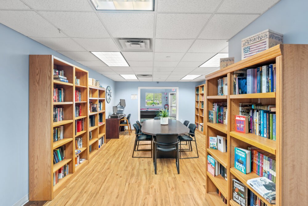 A cozy library study room with bookshelves lining the walls and a central meeting table surrounded by chairs.