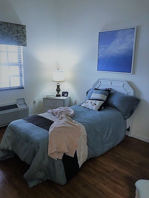 A cozy bedroom with a neatly made bed, featuring pillows and a throw blanket, illuminated by a lamp on the nightstand.
