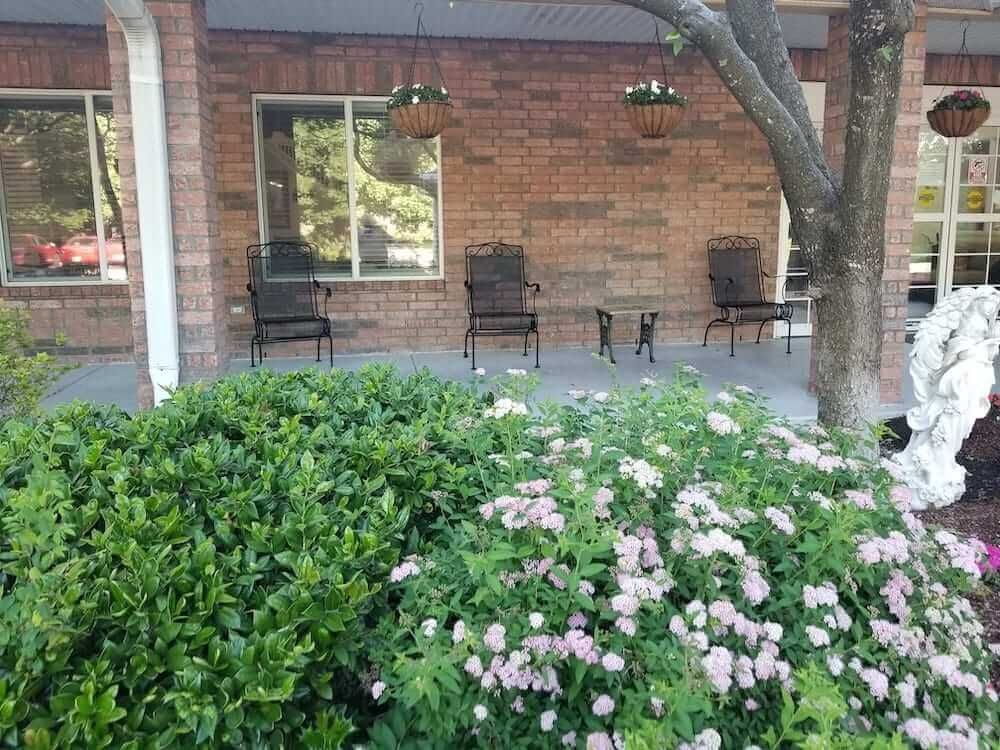 A cozy porch with chairs, hanging plants, and blooming flowers in front.