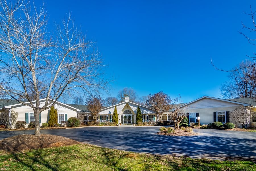 A scenic view of a building with a driveway surrounded by trees and grass under a clear blue sky.