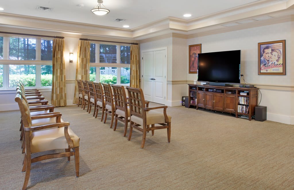A well-lit meeting room with rows of wooden chairs facing a large television.