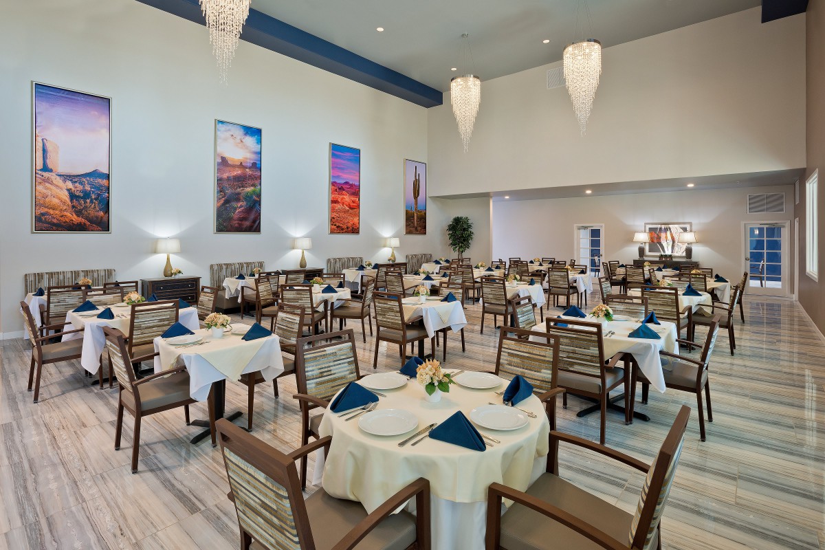 An elegantly set dining room with neatly arranged tables and chairs, featuring decorative napkins and wall art.