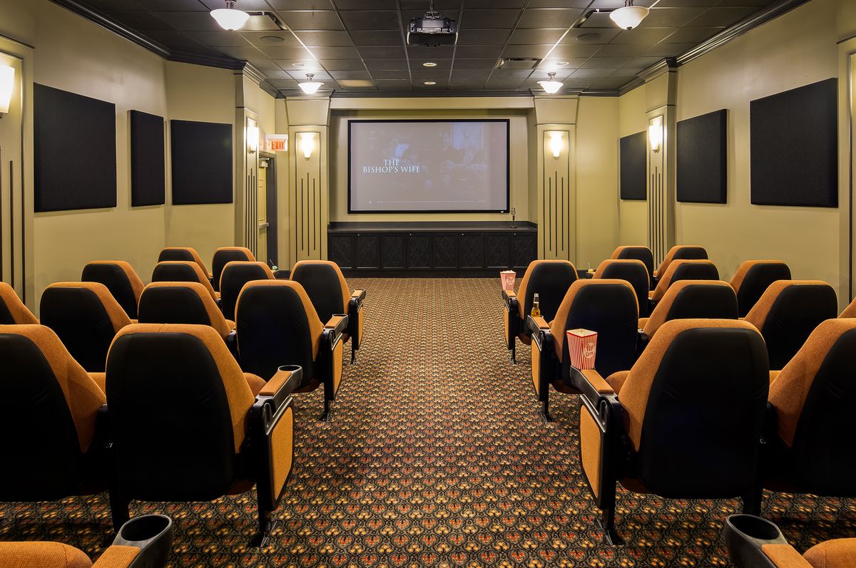 An empty theater room with rows of seats facing a large screen.