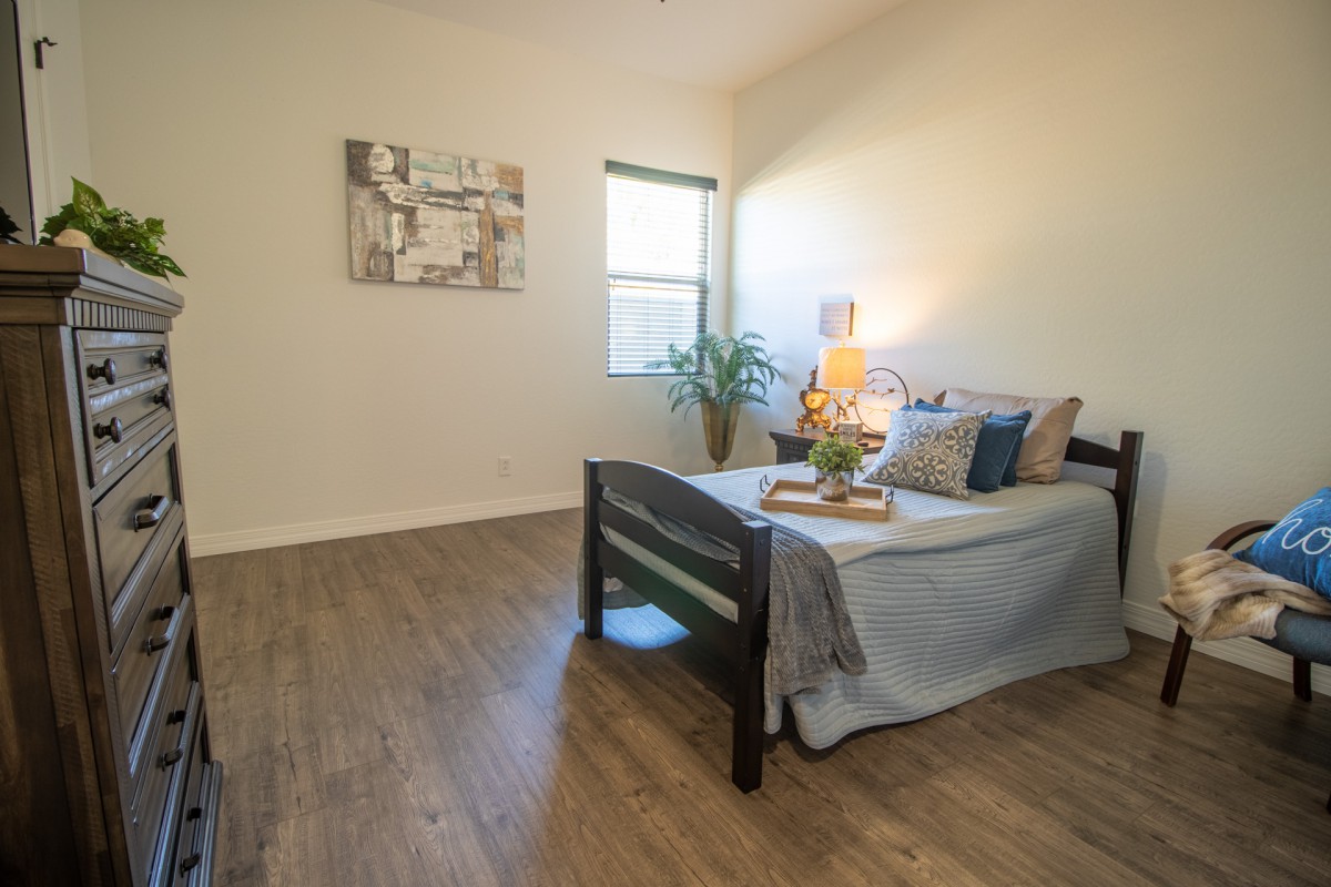 A minimalist bedroom with wooden flooring, simple decor, and ample natural light.
