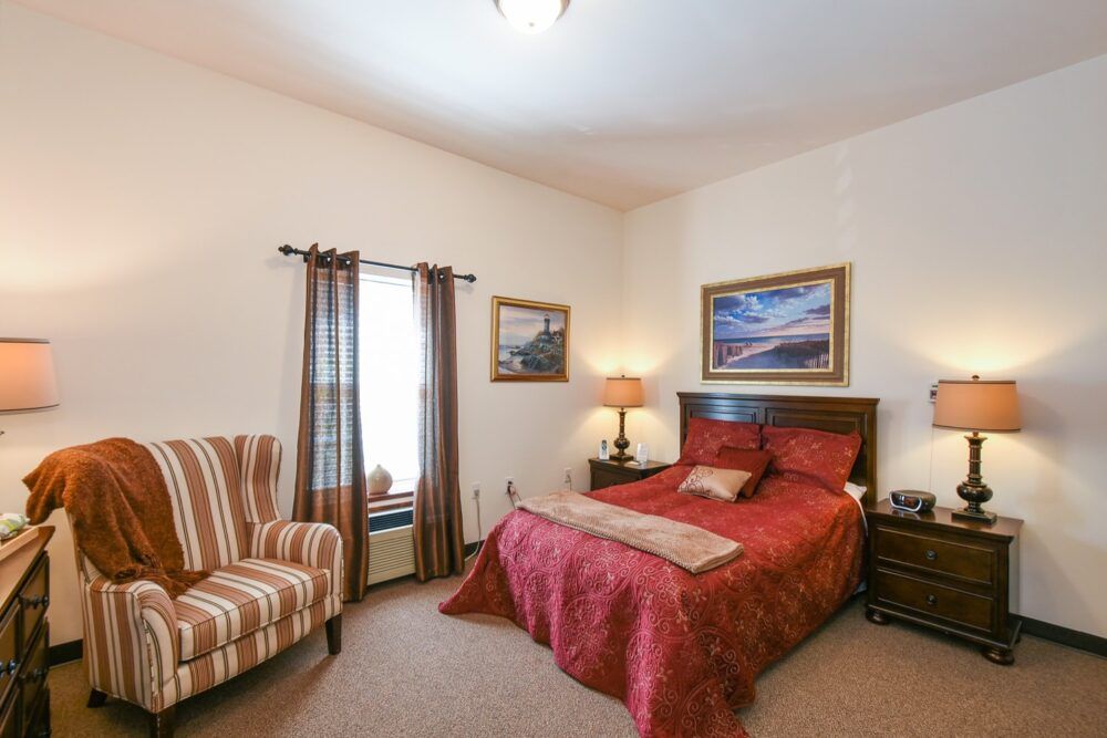 A cozy bedroom with a red bedspread, side tables, and framed artwork on the walls.