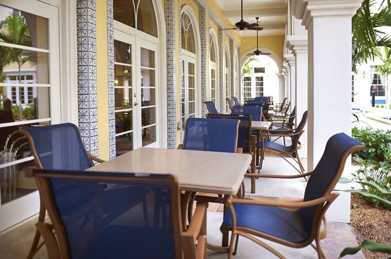A covered outdoor patio with tables and chairs set along a corridor with arched architecture.