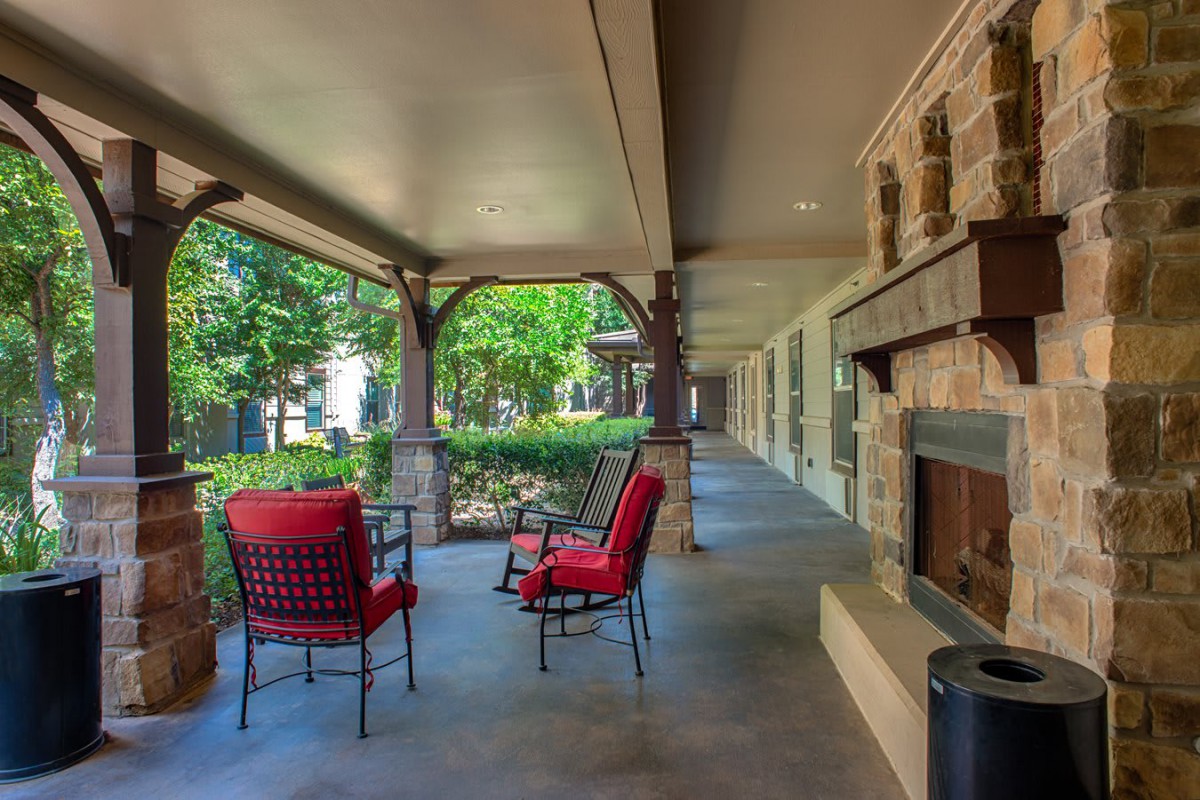 A cozy outdoor patio with red cushioned chairs and a stone fireplace, perfect for relaxation.