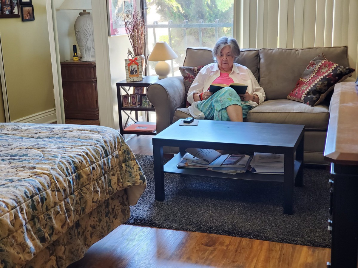 An elderly person sitting on a sofa using a tablet in a cozy living room.