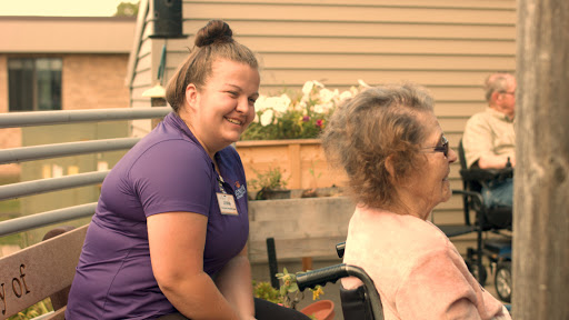 A caregiver shares a joyful moment with an elderly woman in a garden setting.