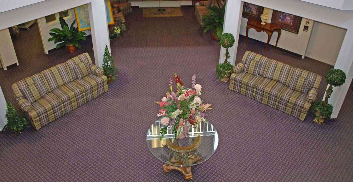 A cozy lobby area featuring a glass table with a floral arrangement, surrounded by patterned sofas and decorative plants.
