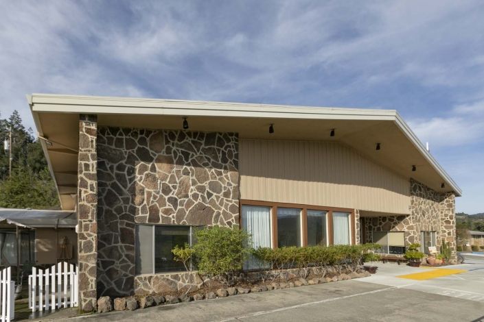 A mid-century modern building with a stone wall and large windows under a blue sky.