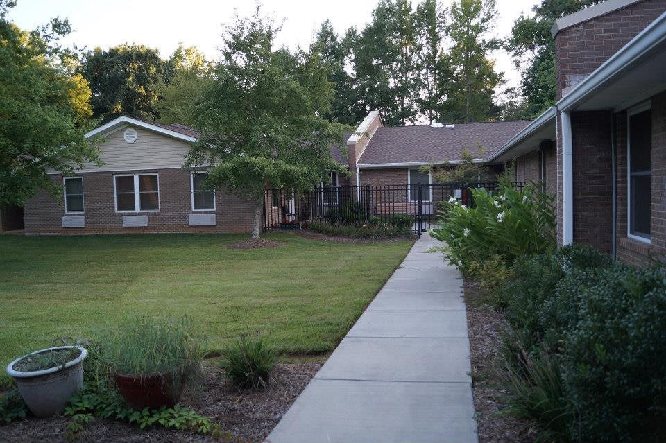 A serene pathway leading to a house surrounded by a well-maintained garden and trees.