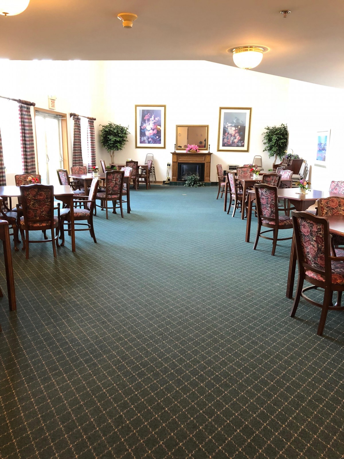 An indoor dining area featuring several tables and chairs, with decorative plants and paintings adorning the space.