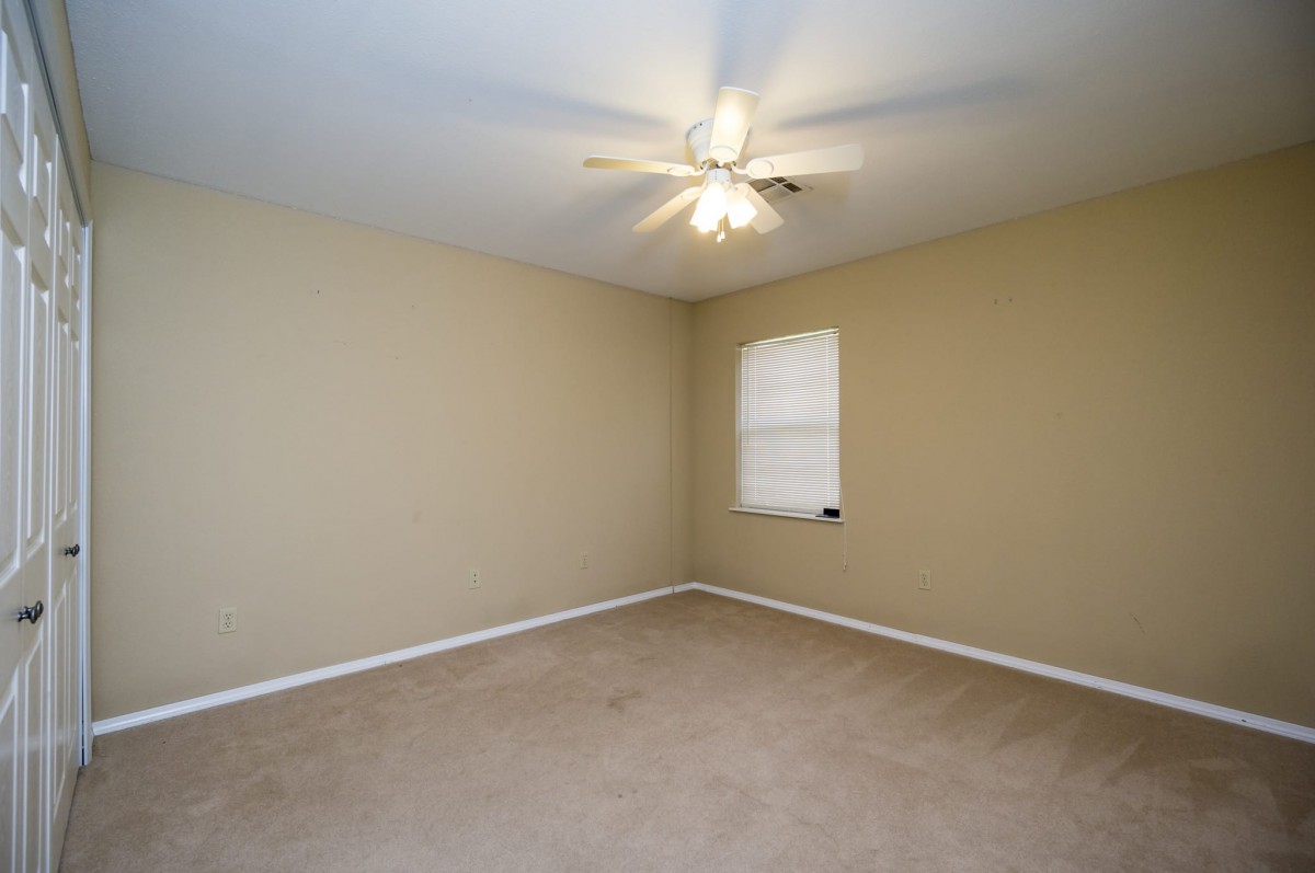 An empty room with beige walls, a ceiling fan, and carpeted floor.