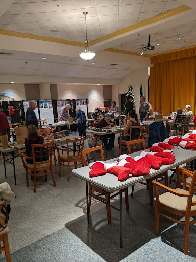 A community gathering with participants engaged in various activities, featuring tables arranged with red hats.