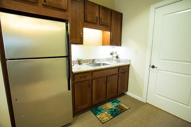 Compact apartment kitchen with wooden cabinets and a stainless steel fridge.