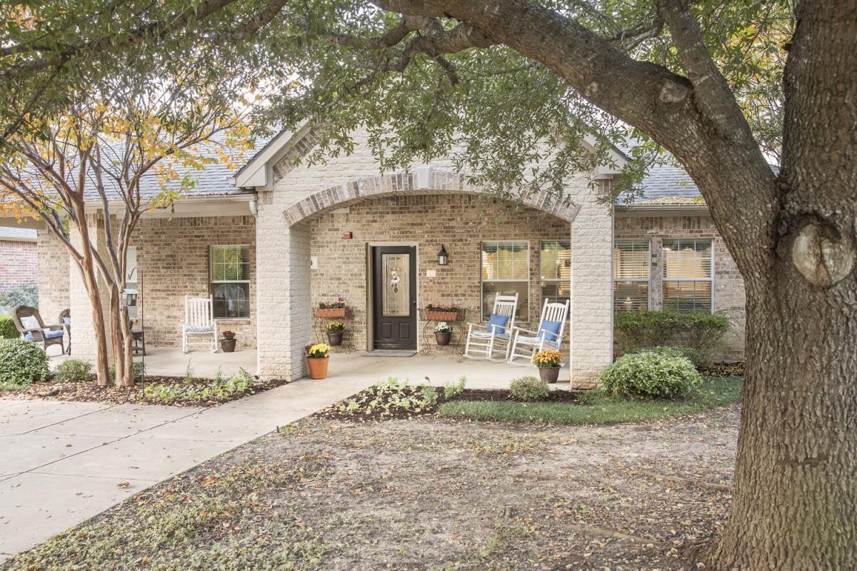 A charming brick house with a cozy front porch and surrounding greenery.