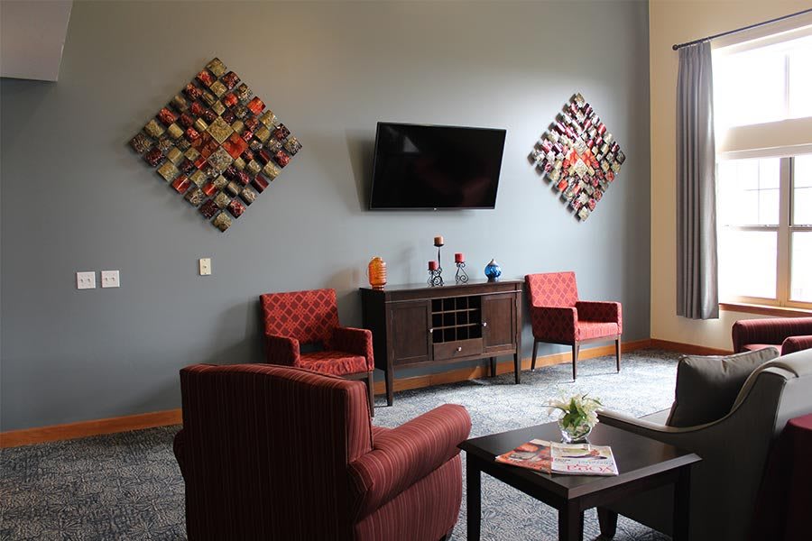 A cozy living room with modern decor, featuring two red chairs, a TV mounted on the wall, and decorative artwork.