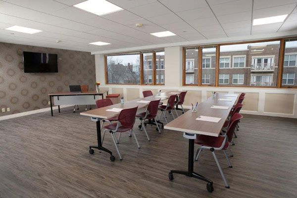 A modern classroom or conference room with arranged tables and chairs, featuring large windows.