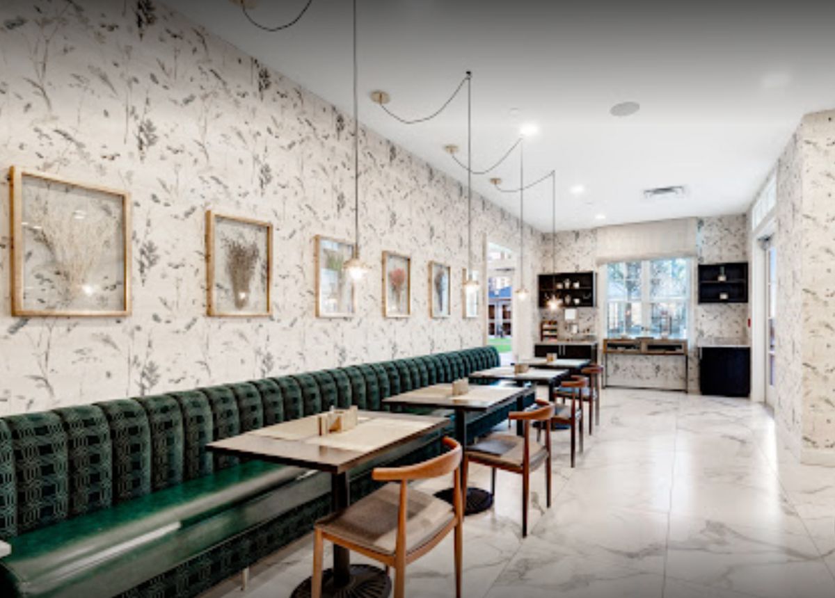 A modern restaurant interior featuring green upholstered seating, stylish lighting fixtures, and wall art.