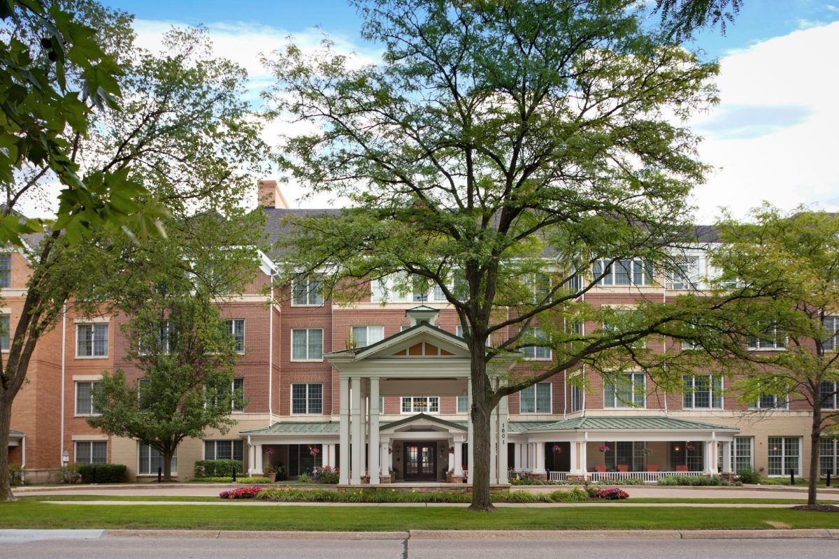 A large brick building with a grand entrance, framed by trees and situated along a street.
