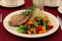 A plated meal featuring a pork chop with a side of mixed vegetables and mashed potatoes, garnished with rosemary.