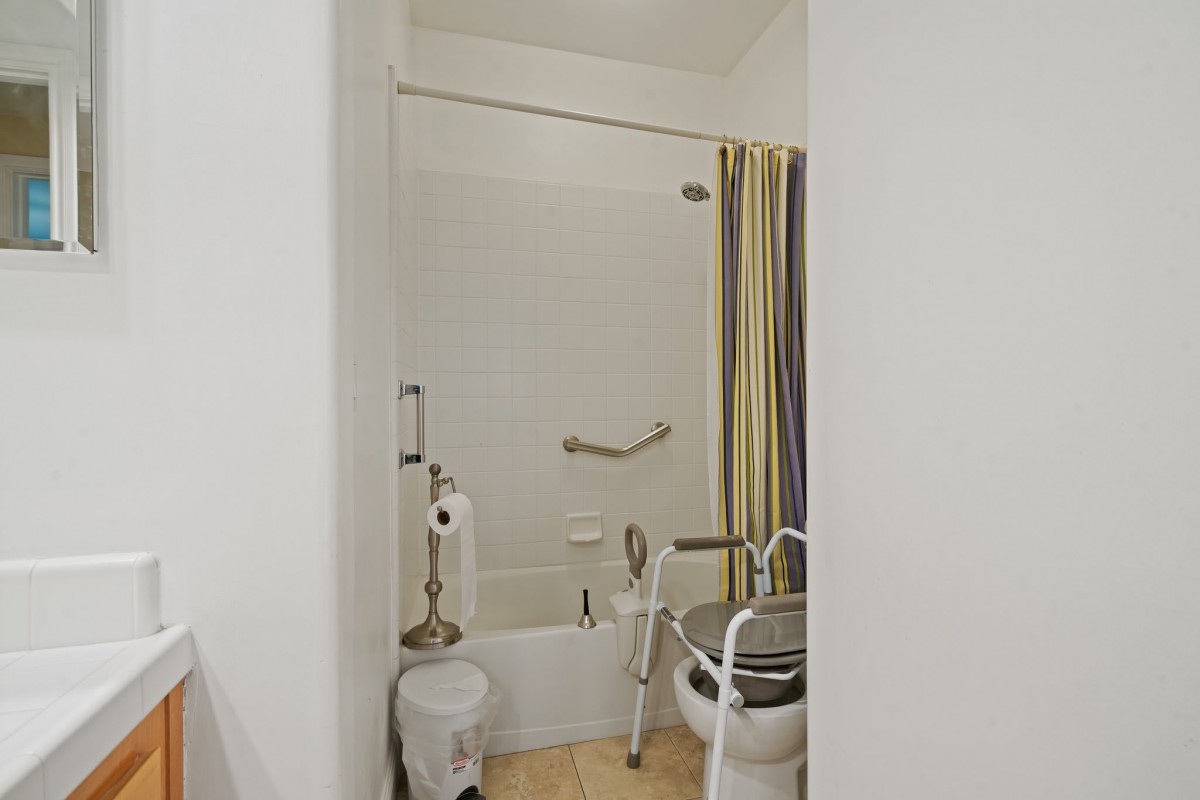 An accessible bathroom with a bathtub, shower curtain, grab bars, and a mobility aid.