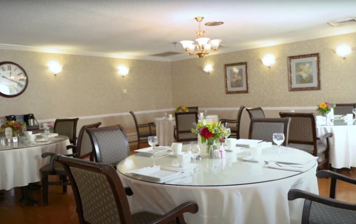 A formal dining room with a round table set for a meal, featuring elegant chairs, a floral centerpiece, and ambient lighting.