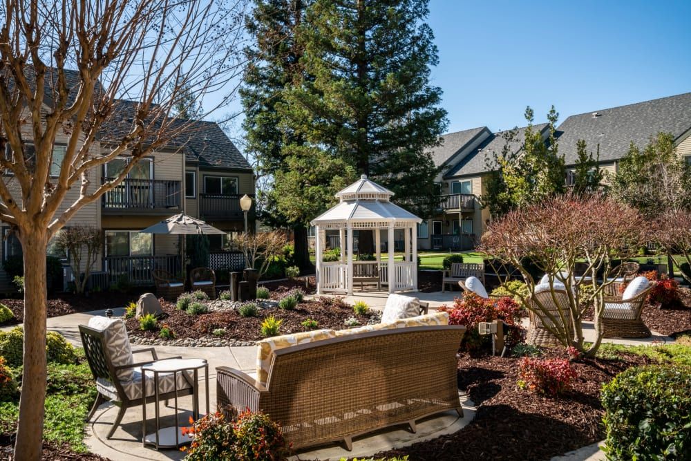 A cozy garden setting with a gazebo and patio furniture surrounded by lush greenery.