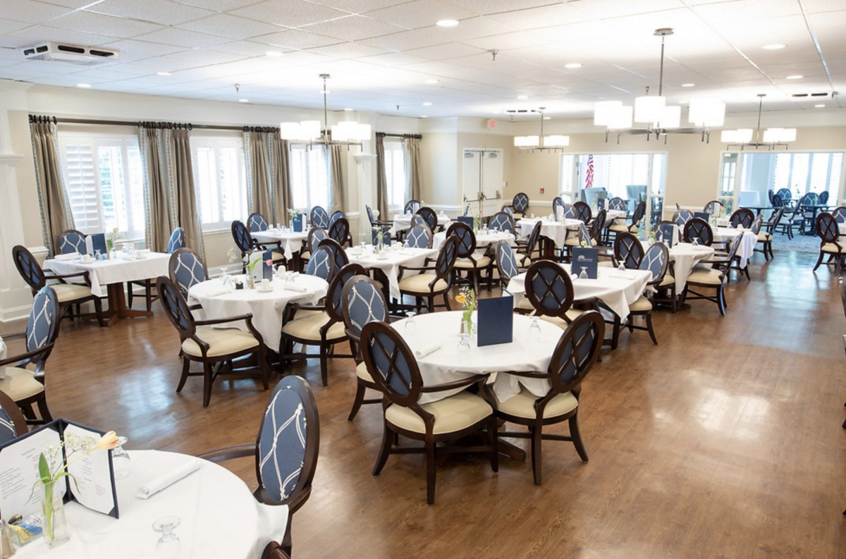 A spacious dining room with elegantly set tables and chairs, featuring white tablecloths and chandeliers.