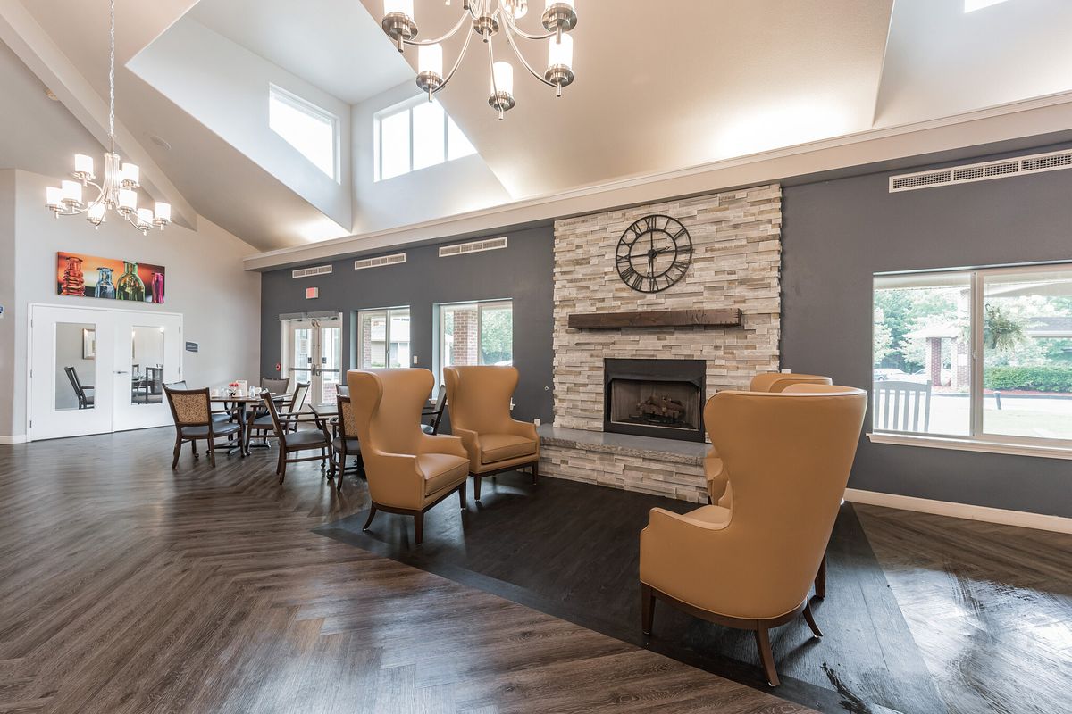A spacious, elegantly designed living room featuring a fireplace with stone accent, surrounded by plush armchairs and illuminated by a modern chandelier.