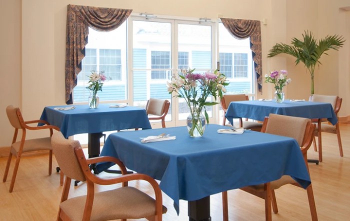A well-lit dining area with blue tablecloths and flower arrangements.
