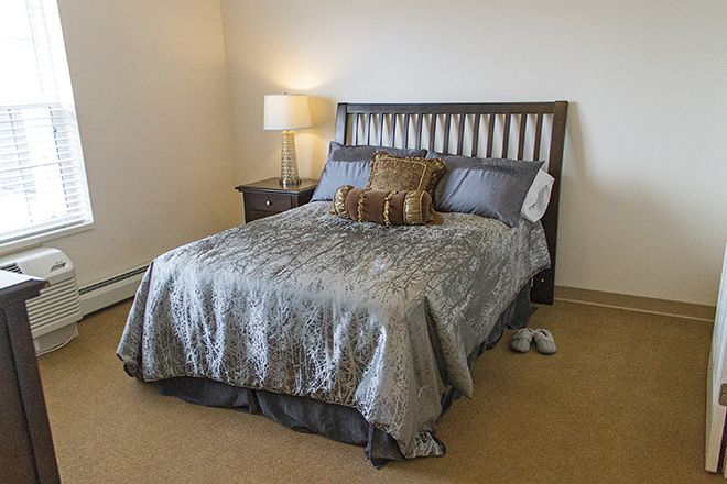 A neatly made bed in a cozy bedroom with a bedside lamp.