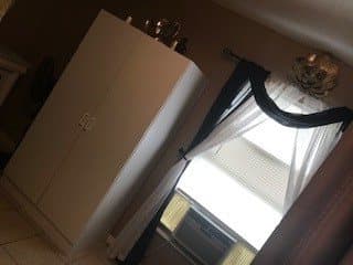 A room with a white wardrobe and a window with curtains, featuring an air conditioner.