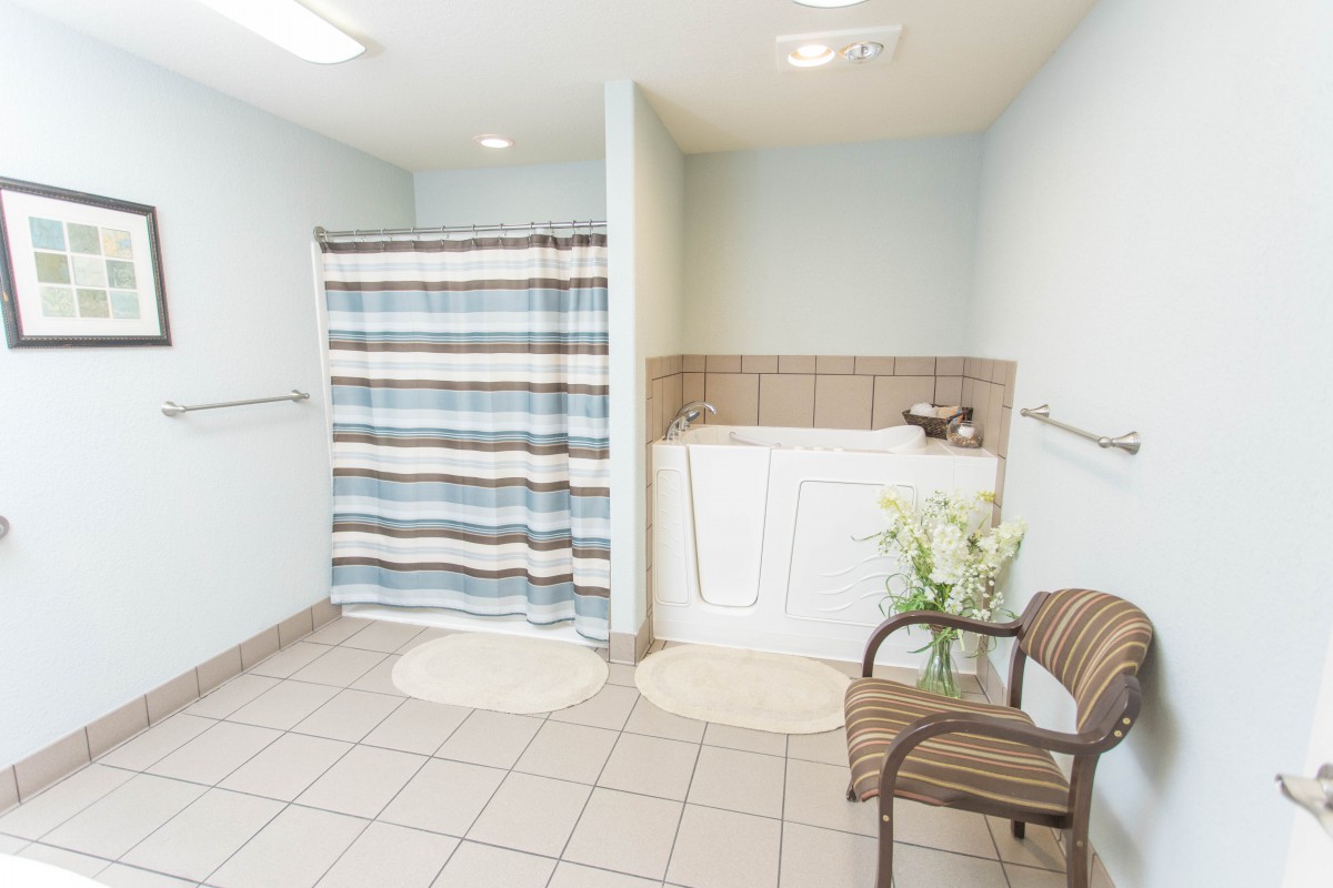 A clean and spacious bathroom with a striped shower curtain, a bathtub, and a comfortable chair.