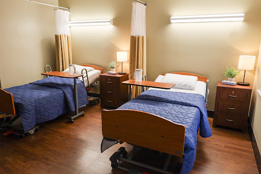 A view of a hospital patient room with two beds and essential furniture.