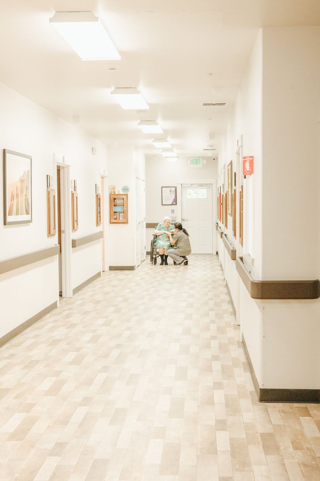 A clean and well-lit hospital corridor with a wheelchair positioned at the end.