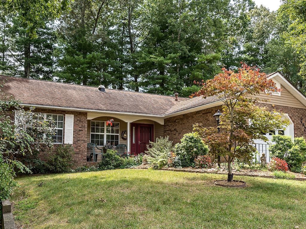 A brick ranch-style house with a well-kept yard and surrounding trees.