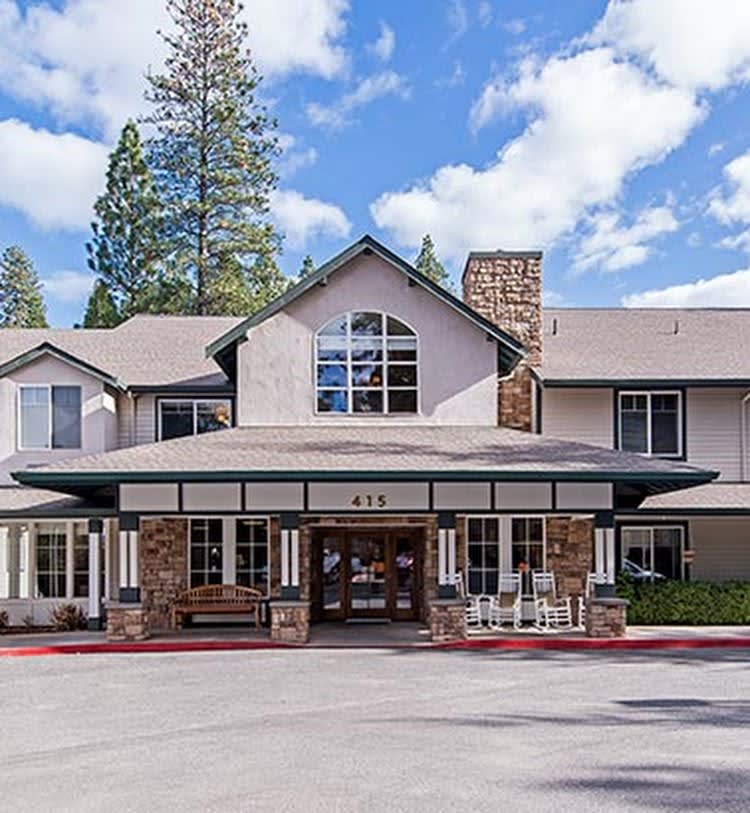 A front view of a building with an entrance, surrounded by trees and a partly cloudy sky.