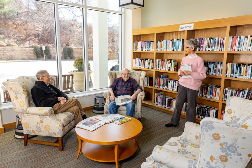 A group of people having a discussion in a library setting with bookshelves in the background.