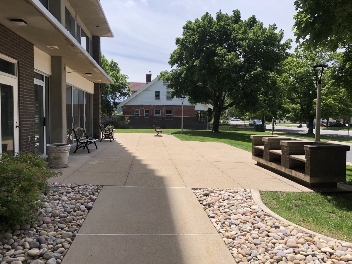 A sunny outdoor setting with a sidewalk bordered by rocks, benches, and trees.
