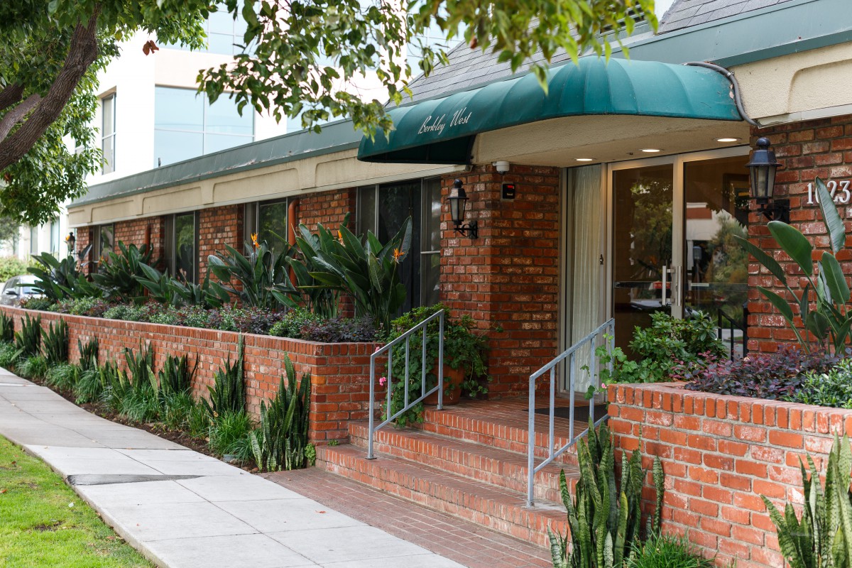 A brick restaurant exterior with green plants and an awning over the entrance.