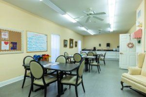 A communal dining area with multiple tables and chairs, a whiteboard on the wall, and a kitchenette in the background.