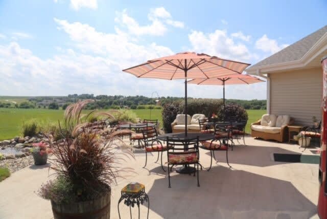 A sunny patio with tables, chairs, and umbrellas overlooking a scenic landscape.
