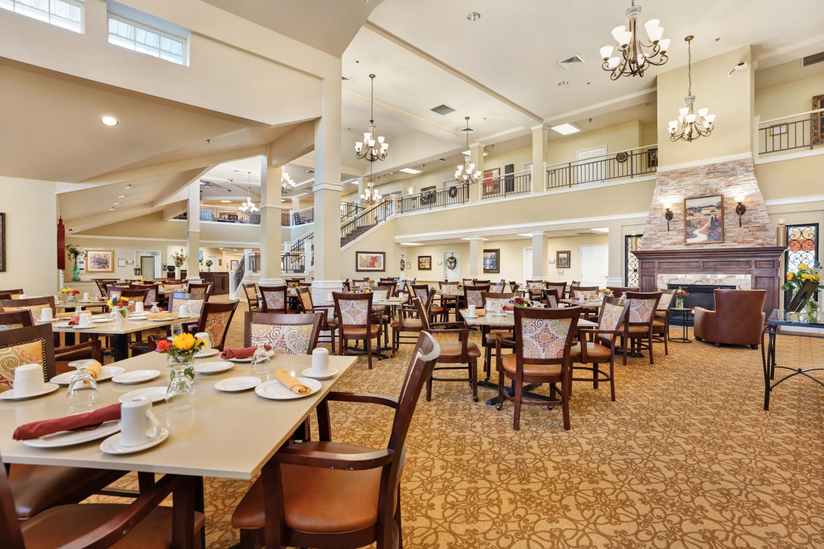 A spacious dining area with elegant decor, featuring tables and chairs arranged under chandeliers.