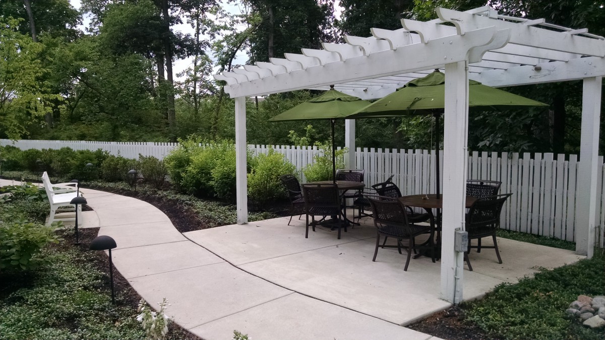 A serene outdoor patio area with a pergola, seating, and garden landscaping.