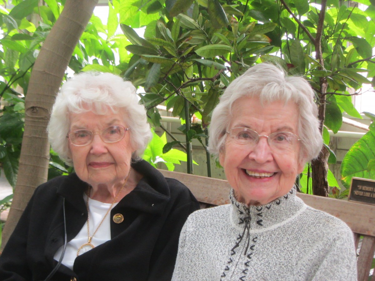 Two elderly women enjoying a day outdoors amidst greenery.